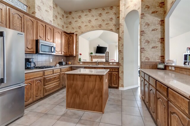 kitchen featuring light tile patterned floors, a center island, light stone counters, stainless steel appliances, and tasteful backsplash