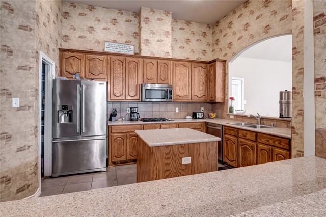 kitchen with backsplash, stainless steel appliances, a kitchen island, sink, and light tile patterned flooring