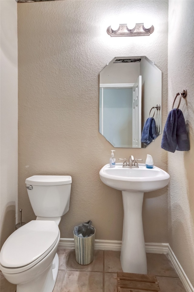 half bathroom with a textured wall, tile patterned flooring, toilet, and baseboards