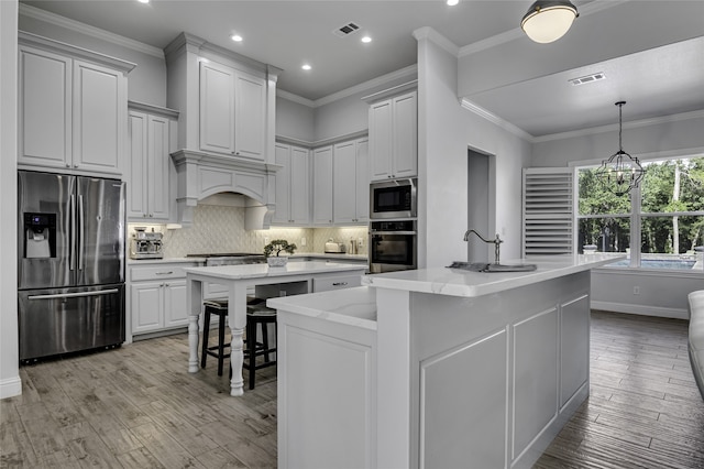 kitchen with backsplash, ornamental molding, light hardwood / wood-style floors, stainless steel appliances, and a center island with sink