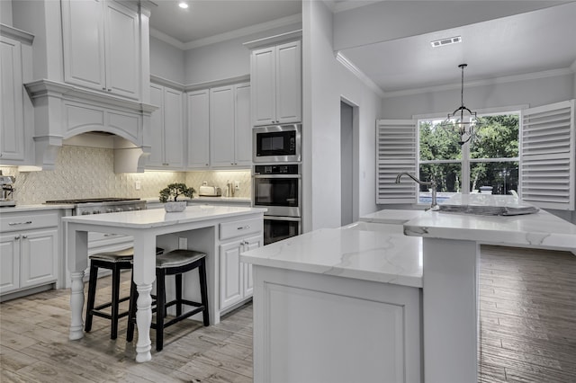 kitchen with light hardwood / wood-style floors, decorative backsplash, stainless steel appliances, and a center island with sink