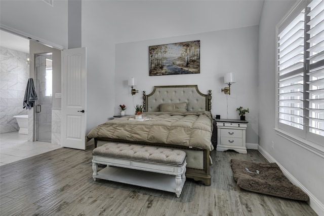 bedroom with connected bathroom, multiple windows, and wood-type flooring