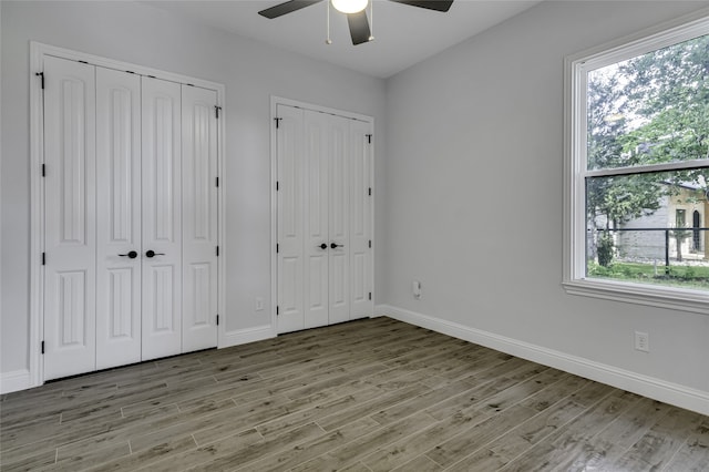 unfurnished bedroom with ceiling fan, multiple windows, two closets, and wood-type flooring