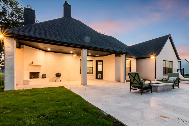 back house at dusk featuring a patio, a fire pit, and a lawn