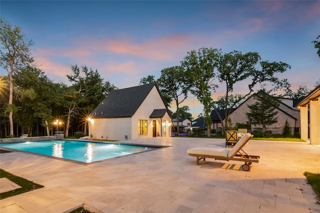 pool at dusk with pool water feature and a patio area