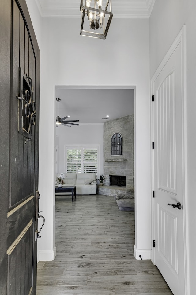 foyer with crown molding, ceiling fan with notable chandelier, a stone fireplace, and wood-type flooring