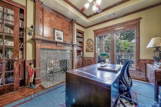 home office with built in shelves, a wainscoted wall, visible vents, ornamental molding, and a raised ceiling