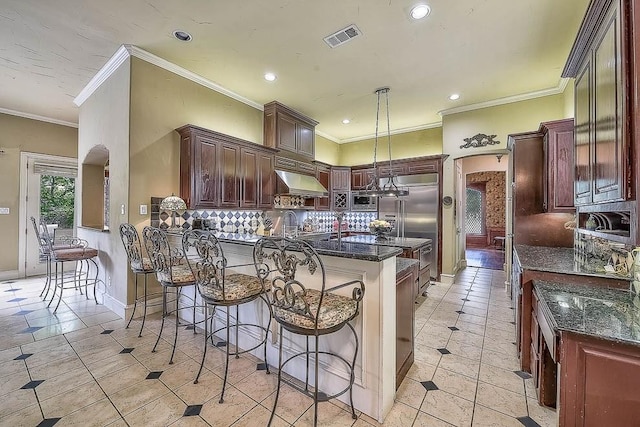 kitchen featuring arched walkways, decorative light fixtures, visible vents, decorative backsplash, and dark stone countertops