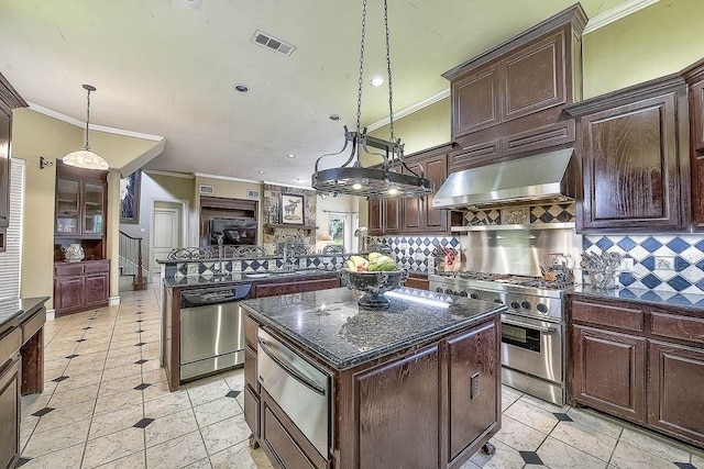 kitchen with visible vents, appliances with stainless steel finishes, decorative light fixtures, a center island, and wall chimney range hood