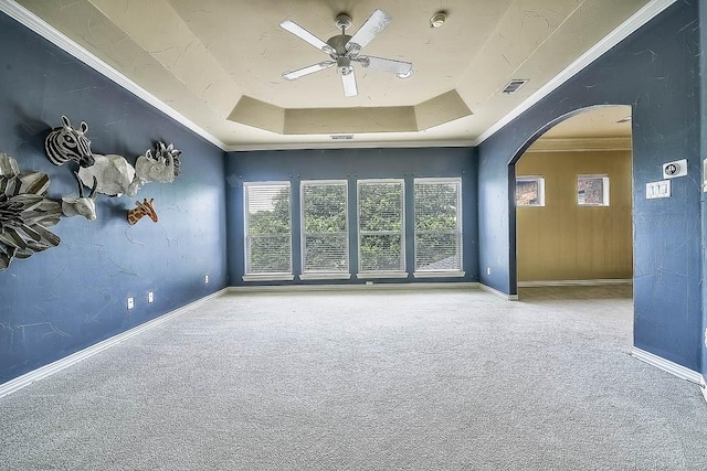 carpeted empty room with arched walkways, a raised ceiling, a ceiling fan, and baseboards