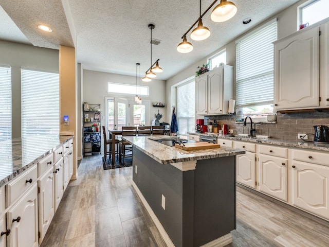 kitchen with a center island, pendant lighting, white cabinetry, and light stone countertops