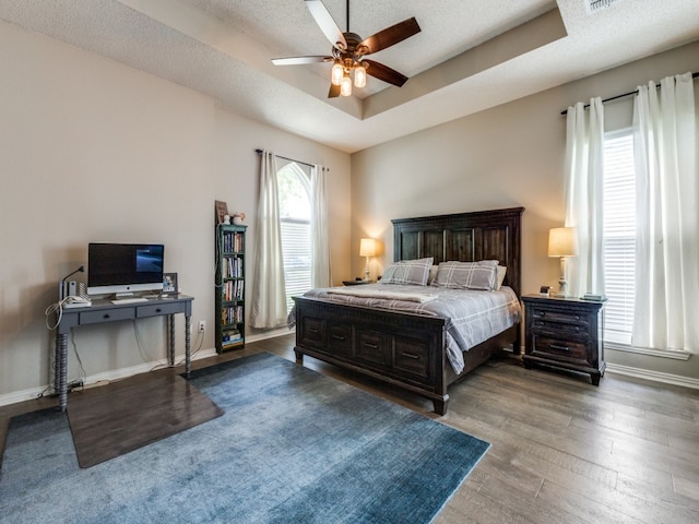 bedroom featuring a tray ceiling, hardwood / wood-style floors, a textured ceiling, and ceiling fan