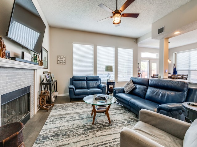 living room featuring dark hardwood / wood-style flooring, ceiling fan, a brick fireplace, and a textured ceiling