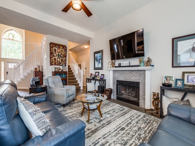 living room with a brick fireplace, hardwood / wood-style flooring, ceiling fan, and a textured ceiling