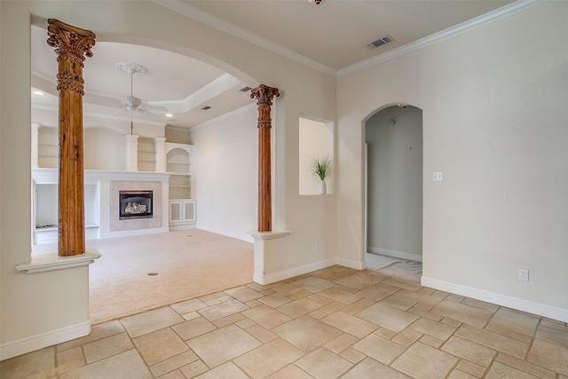 unfurnished room with ceiling fan, built in features, a tile fireplace, light colored carpet, and crown molding