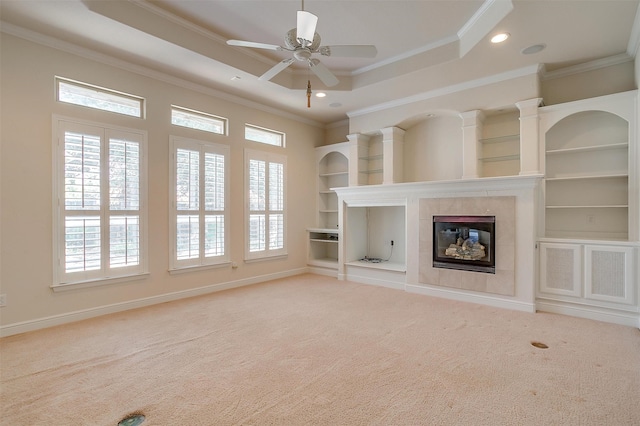 unfurnished living room featuring a tile fireplace, ceiling fan, built in shelves, ornamental molding, and light carpet