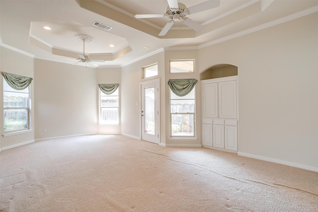 carpeted spare room featuring a raised ceiling, crown molding, ceiling fan, and plenty of natural light