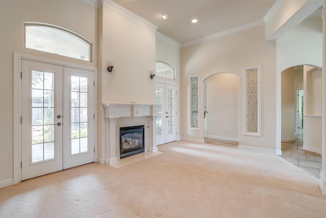 unfurnished living room featuring ornamental molding, french doors, a tiled fireplace, light carpet, and a towering ceiling