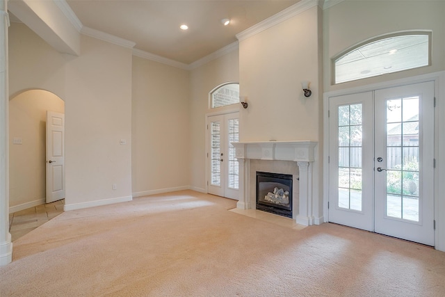 unfurnished living room with light carpet, a high ceiling, ornamental molding, and french doors