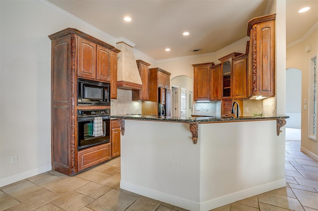 kitchen featuring dark stone countertops, backsplash, kitchen peninsula, black appliances, and premium range hood