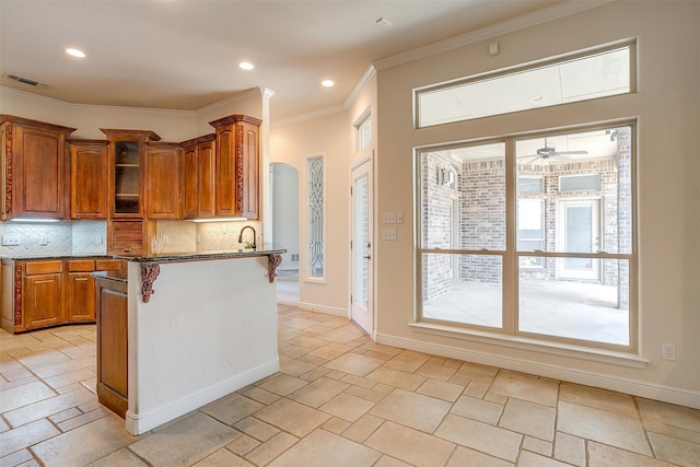 kitchen featuring ceiling fan, dark stone counters, crown molding, a kitchen bar, and decorative backsplash