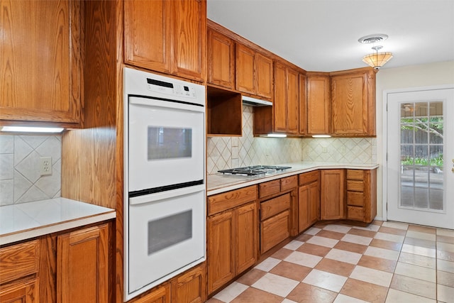 kitchen with white double oven, pendant lighting, stainless steel gas cooktop, and tasteful backsplash