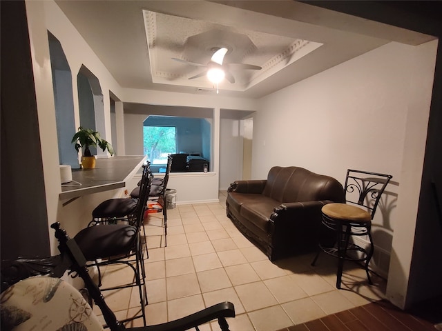 tiled living room with a raised ceiling and ceiling fan