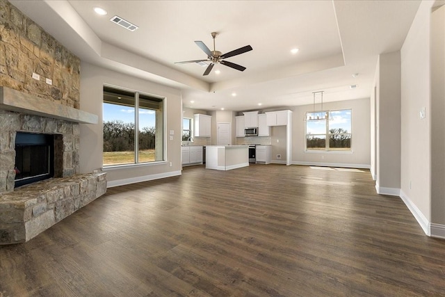 unfurnished living room with a ceiling fan, visible vents, dark wood-style flooring, a stone fireplace, and a raised ceiling