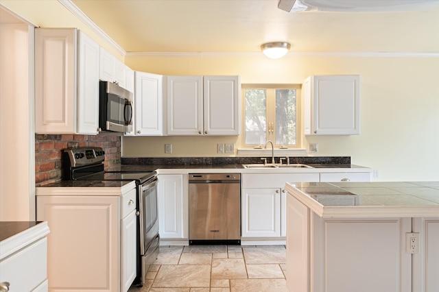 kitchen featuring light tile patterned floors, ornamental molding, appliances with stainless steel finishes, tile countertops, and white cabinetry