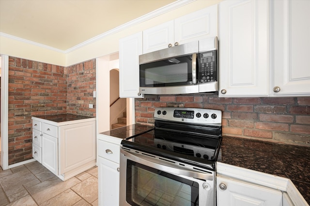 kitchen featuring light tile patterned floors, stainless steel appliances, brick wall, and white cabinets