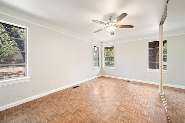 empty room featuring a wealth of natural light, ceiling fan, ornamental molding, and light parquet floors