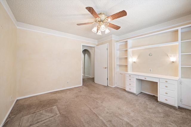 unfurnished bedroom with ceiling fan, built in desk, light colored carpet, and a textured ceiling