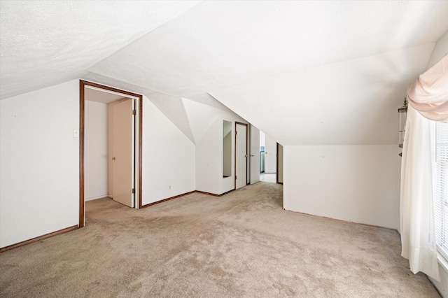 additional living space featuring a textured ceiling, light carpet, and lofted ceiling