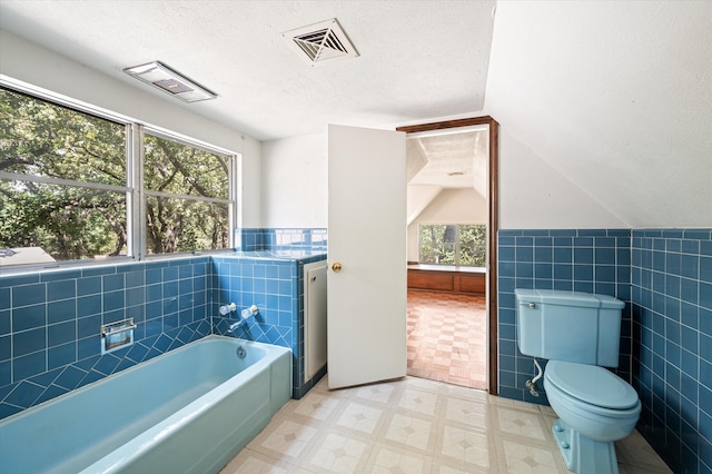 bathroom featuring a washtub, tile walls, lofted ceiling, and tile patterned flooring