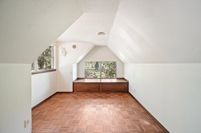 bonus room with light parquet flooring, a textured ceiling, lofted ceiling, and plenty of natural light