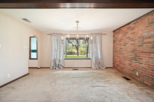 carpeted spare room featuring a notable chandelier and brick wall