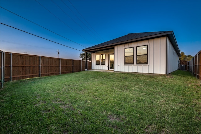 back house at dusk with central AC unit and a lawn