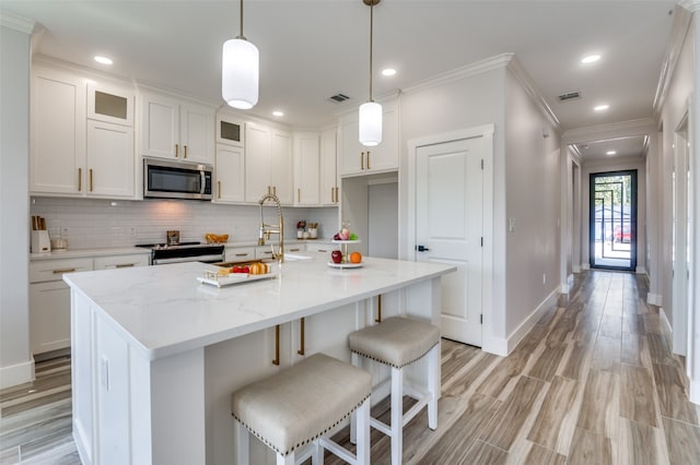 kitchen with light stone countertops, crown molding, a kitchen island with sink, and white cabinets