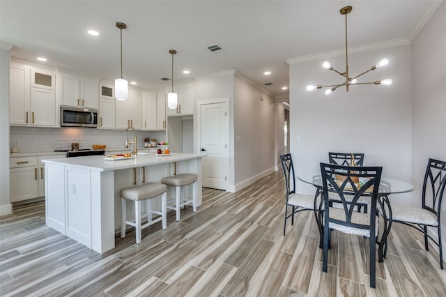 kitchen featuring white cabinets, a kitchen island with sink, stainless steel appliances, and hanging light fixtures