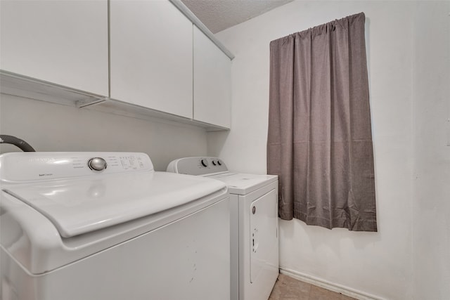 washroom with a textured ceiling, light tile patterned flooring, cabinets, and washing machine and clothes dryer