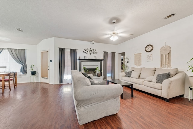 living room with ceiling fan, a fireplace, a textured ceiling, and wood-type flooring