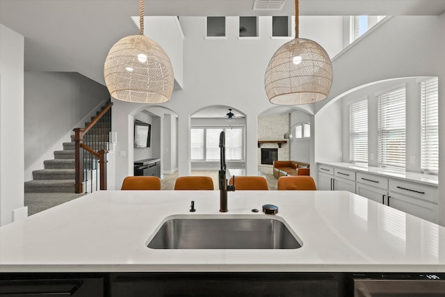 kitchen featuring ceiling fan, pendant lighting, sink, a kitchen island with sink, and a fireplace