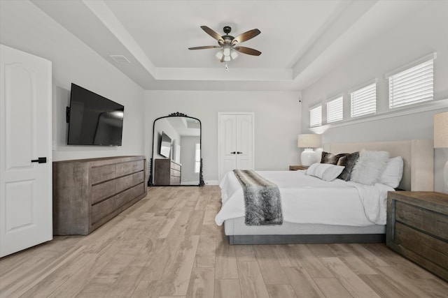 bedroom with ceiling fan, a raised ceiling, and light hardwood / wood-style floors