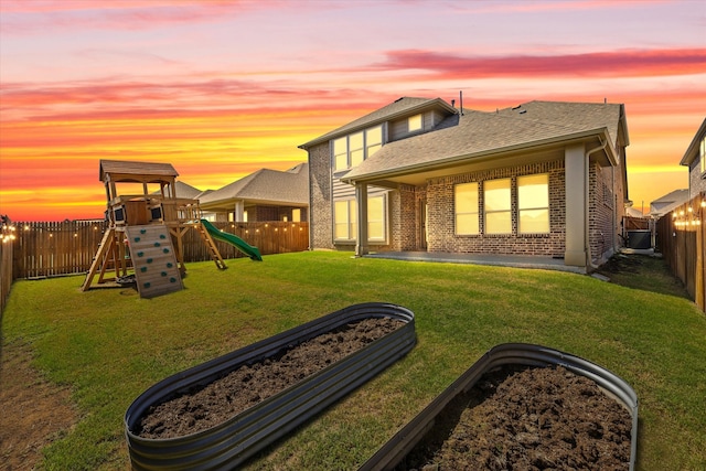 back house at dusk featuring a playground, a lawn, and a patio area