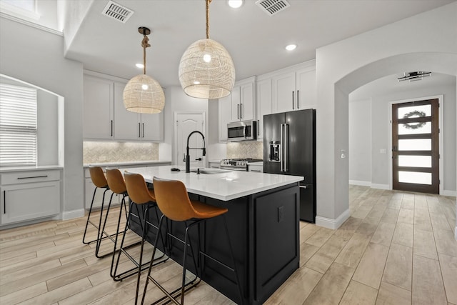 kitchen featuring sink, white cabinetry, light hardwood / wood-style flooring, stainless steel appliances, and a center island with sink