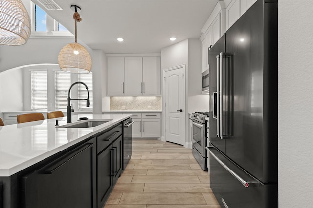 kitchen with light wood-type flooring, sink, white cabinetry, stainless steel appliances, and decorative light fixtures