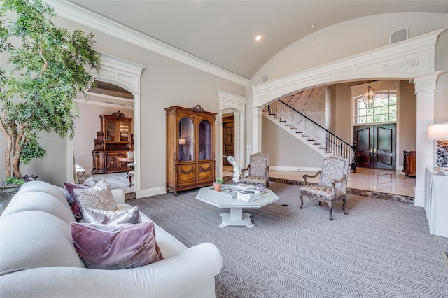 carpeted living room with a towering ceiling, ornamental molding, a chandelier, and ornate columns