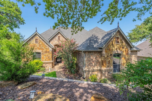 view of front of home with stone siding, brick siding, and roof with shingles