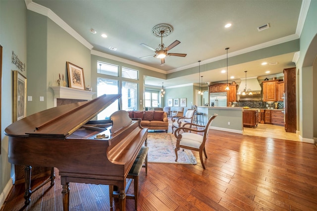 living area with baseboards, visible vents, a ceiling fan, light wood-style flooring, and crown molding