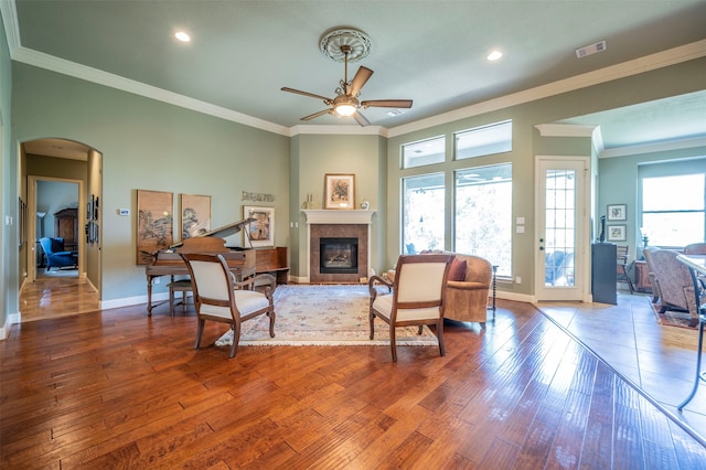 living room with ceiling fan, a tiled fireplace, wood-type flooring, and crown molding